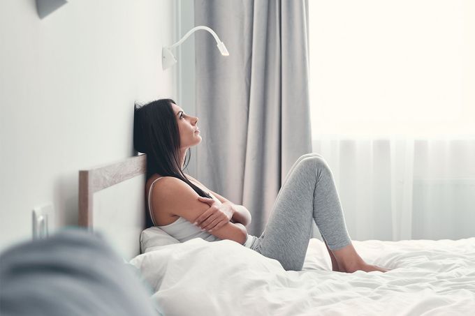A woman is sitting on a bed leaning against a wall