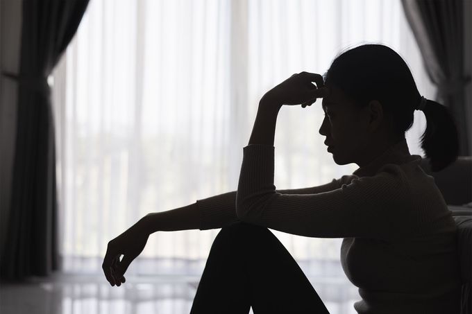 A silhouette of a woman sitting on a couch in front of a window