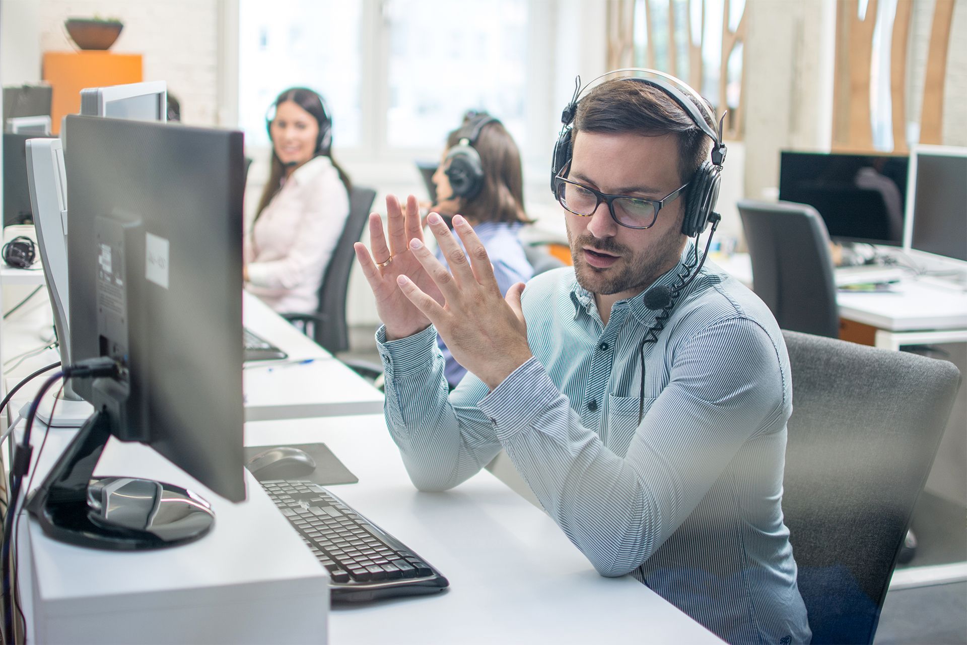 Man with headset gestures while looking at computer in office setting.