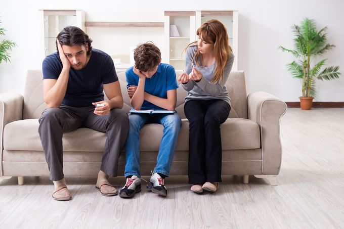 A family is sitting on a couch looking at a tablet.