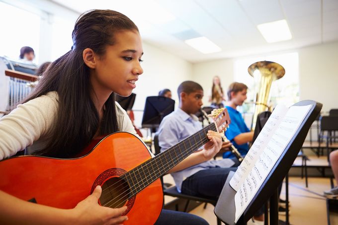 A girl is playing a guitar in a classroom with other students.