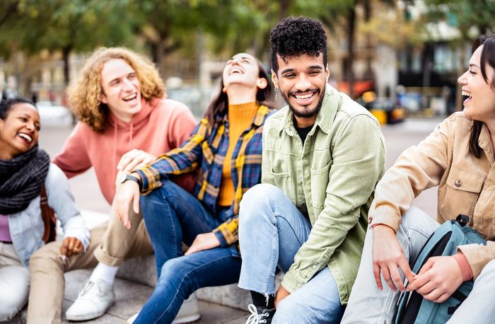 A group of young people are sitting on the ground laughing.