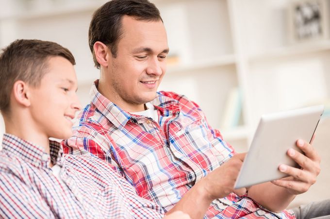 A man and a boy are sitting on a couch looking at a tablet.