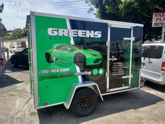 Green mobile detailing trailer with a car graphic, parked on a street.