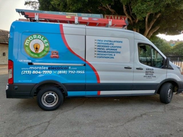 Morales Electrical van with ladder on top, blue and white wrap, parked on a street.