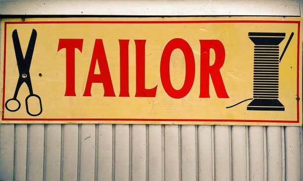 Sign for a tailor shop with scissors and spool of thread; red text on a yellow background.