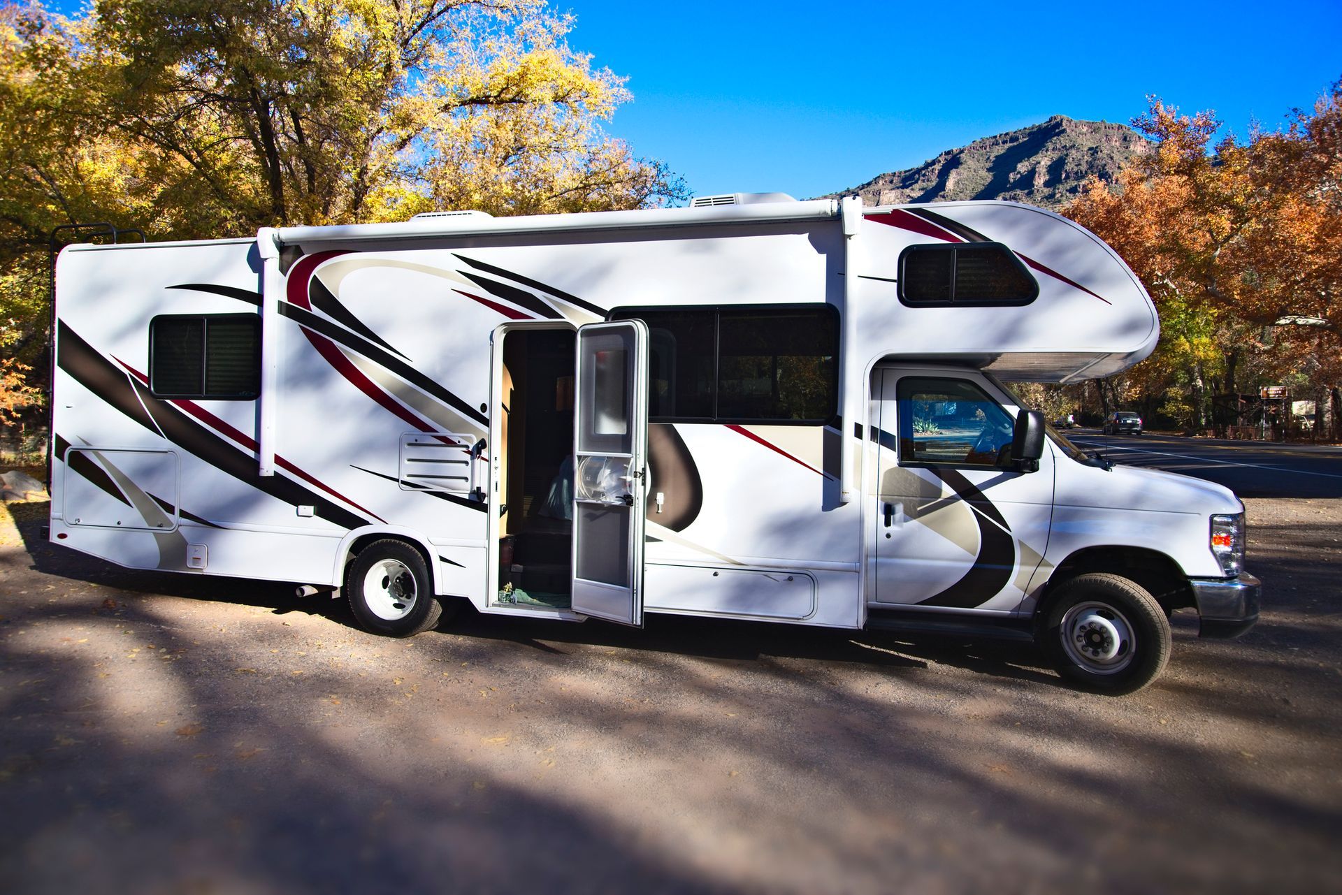 White RV parked outdoors, door open. Trees with fall foliage, mountain background.