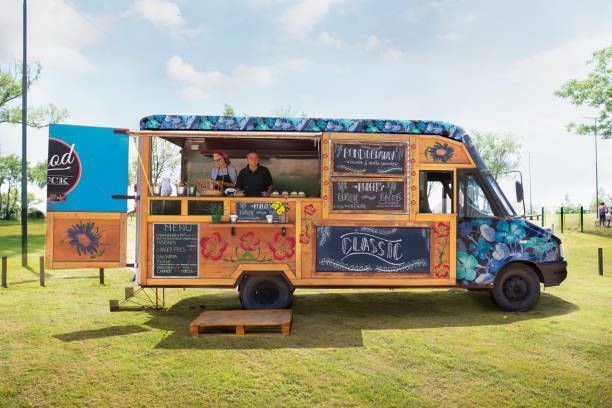 Food truck with two people, wooden facade, serving food outdoors on a sunny day.