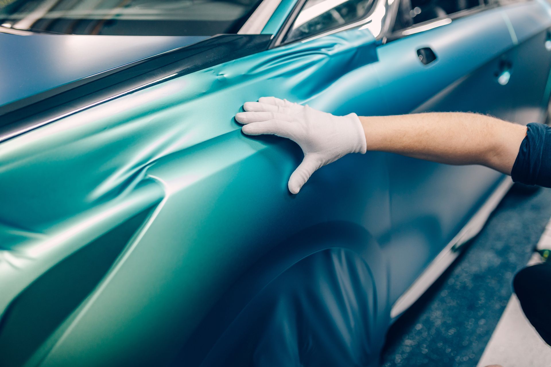 Gloved hand smoothing teal car wrap on a vehicle's side panel.