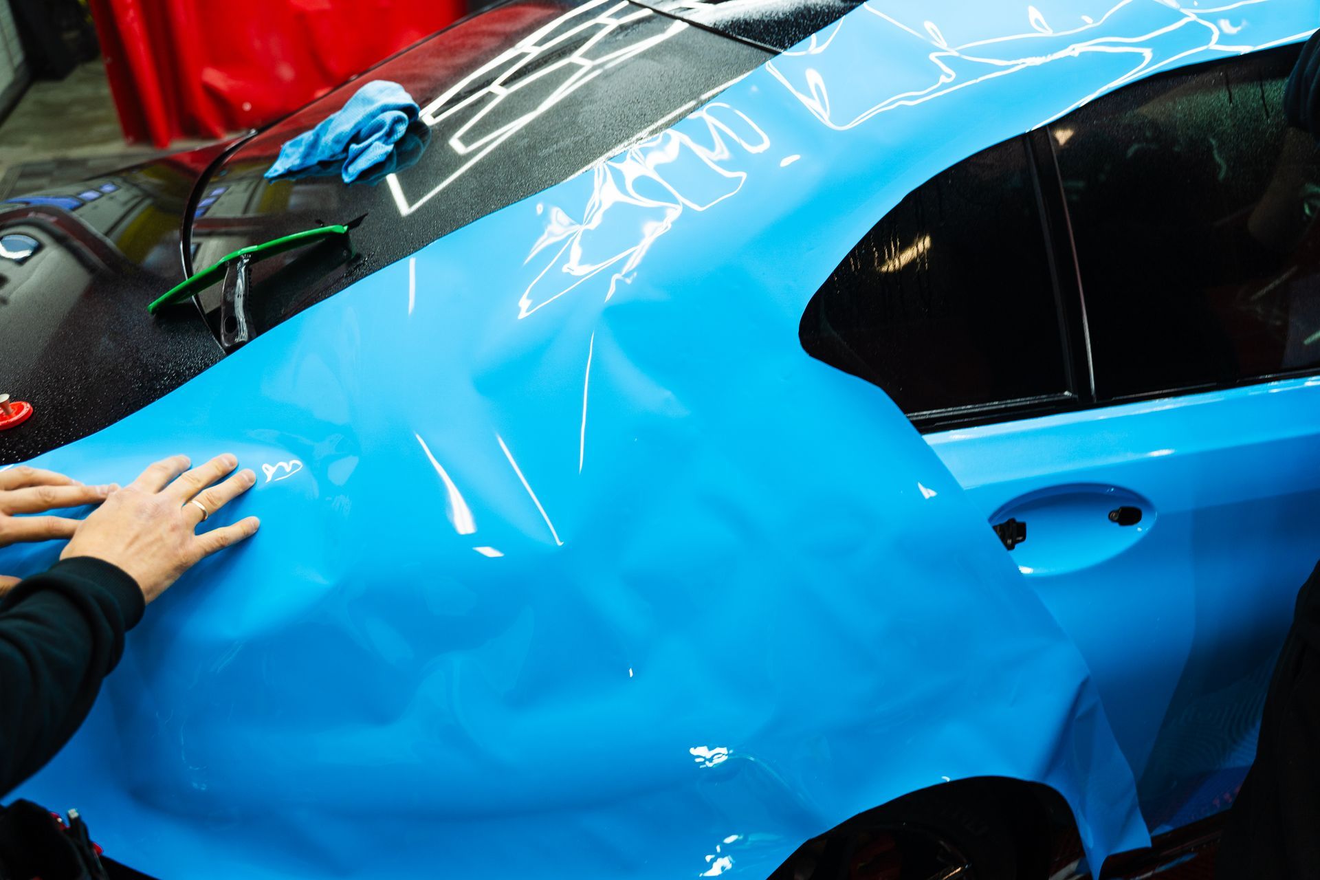 Blue car being wrapped; hands smoothing vinyl. Blue car being wrapped; hands smoothing vinyl.