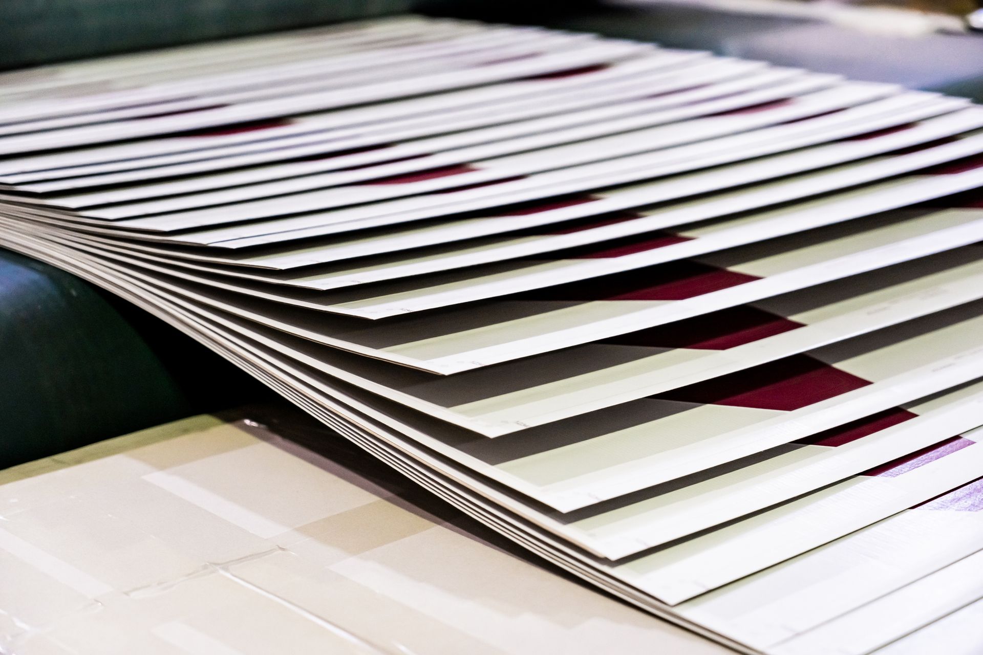 Sheets of printed paper stacked and fanned out on a machine, with a maroon design visible.