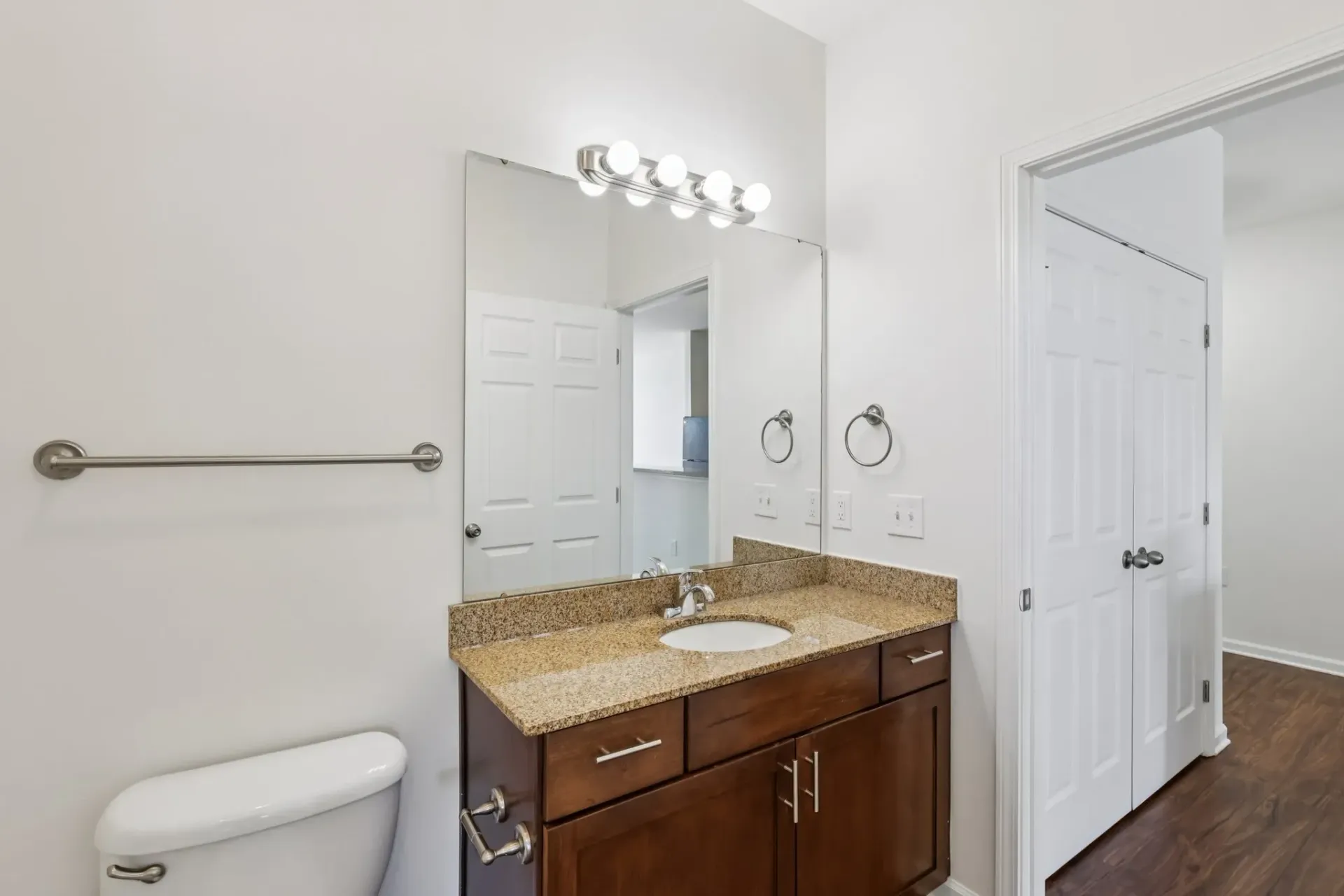 Bathroom vanity with granite countertop, sink, mirror, and toilet.