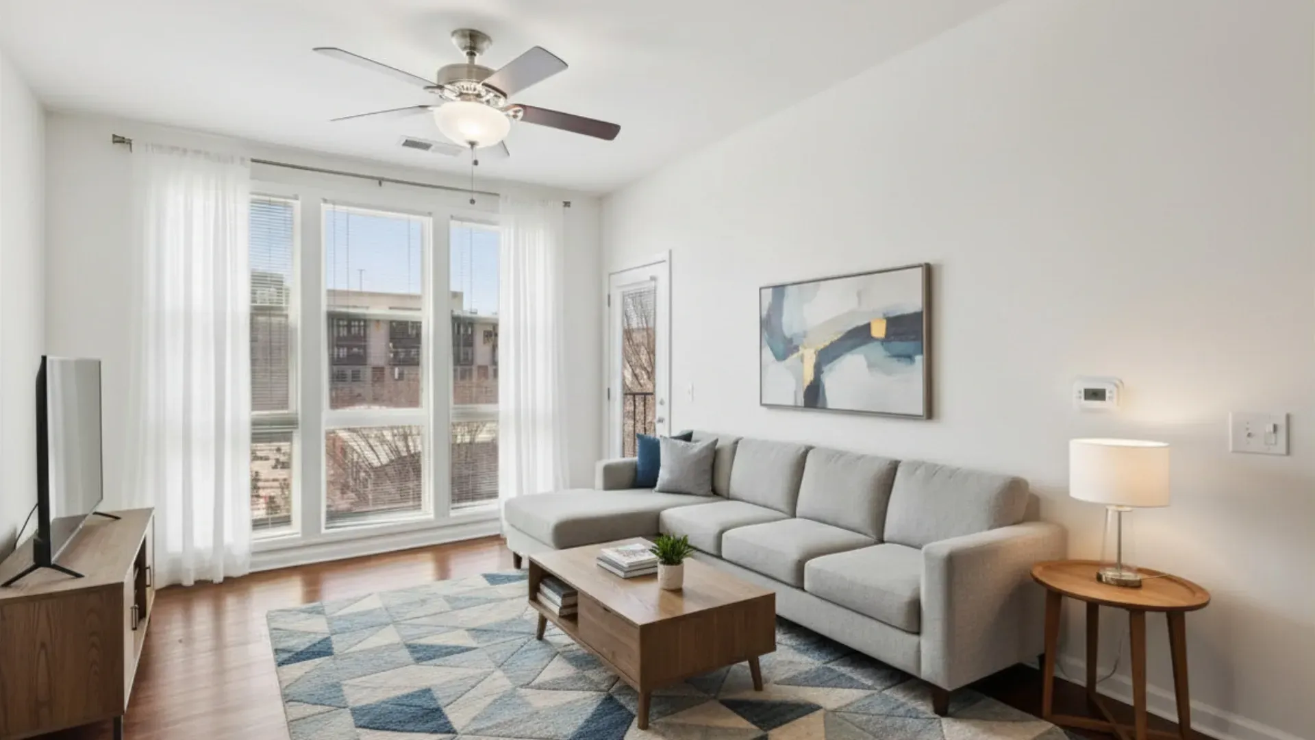Bright living room with a sectional sofa, coffee table, TV, and large windows.