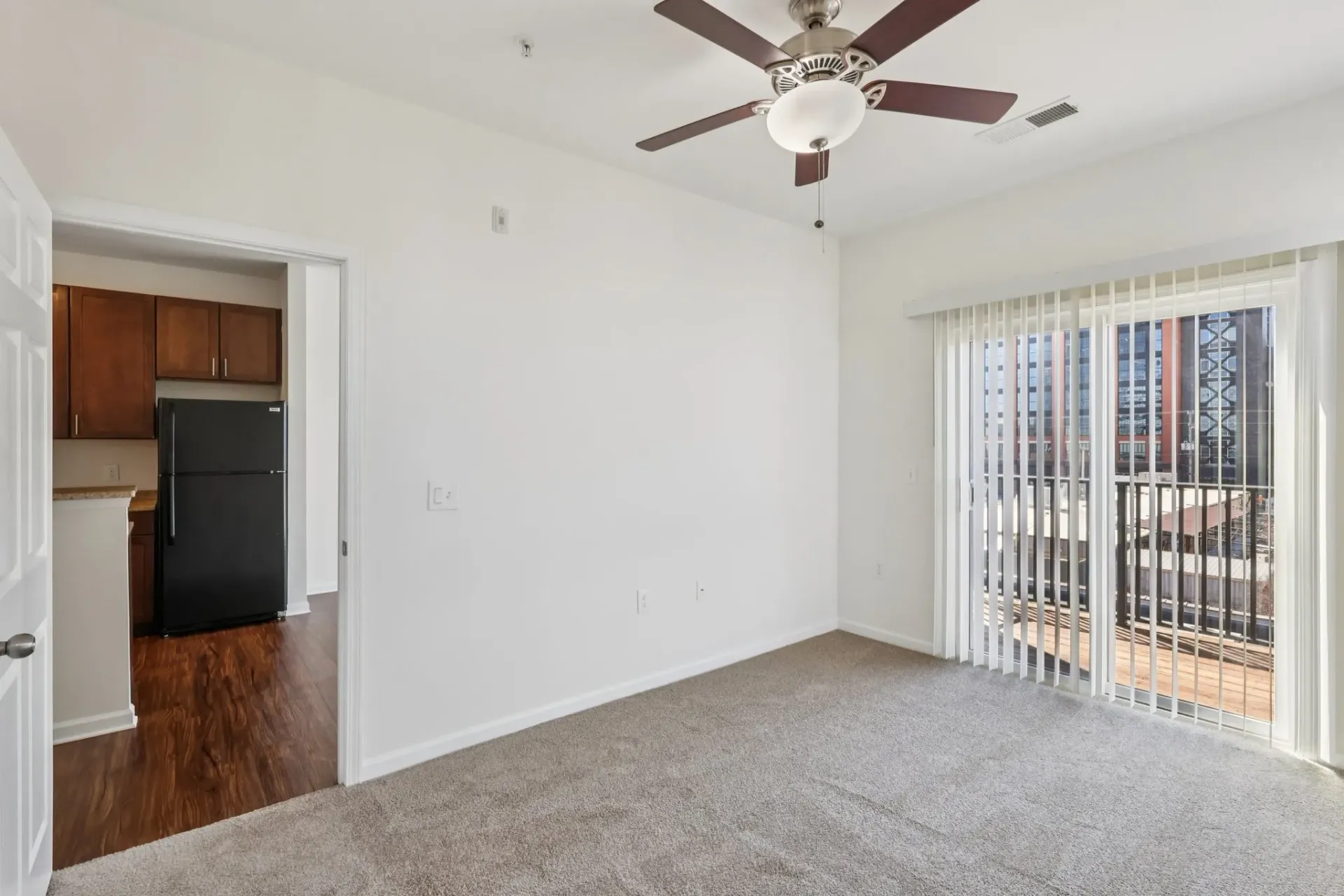 Living room with carpet, ceiling fan, and balcony access. Kitchen visible through doorway.