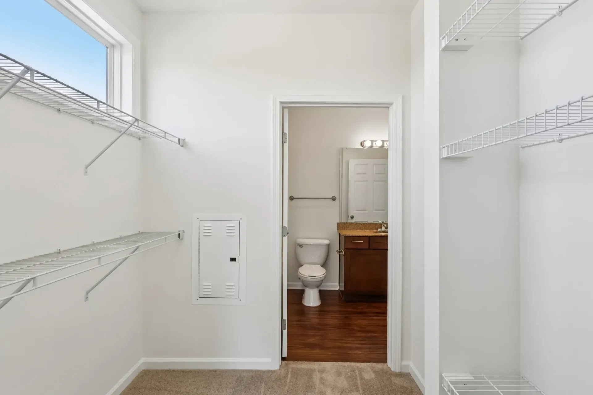 Walk-in closet with built-in shelves and a view into the bathroom with toilet and vanity.