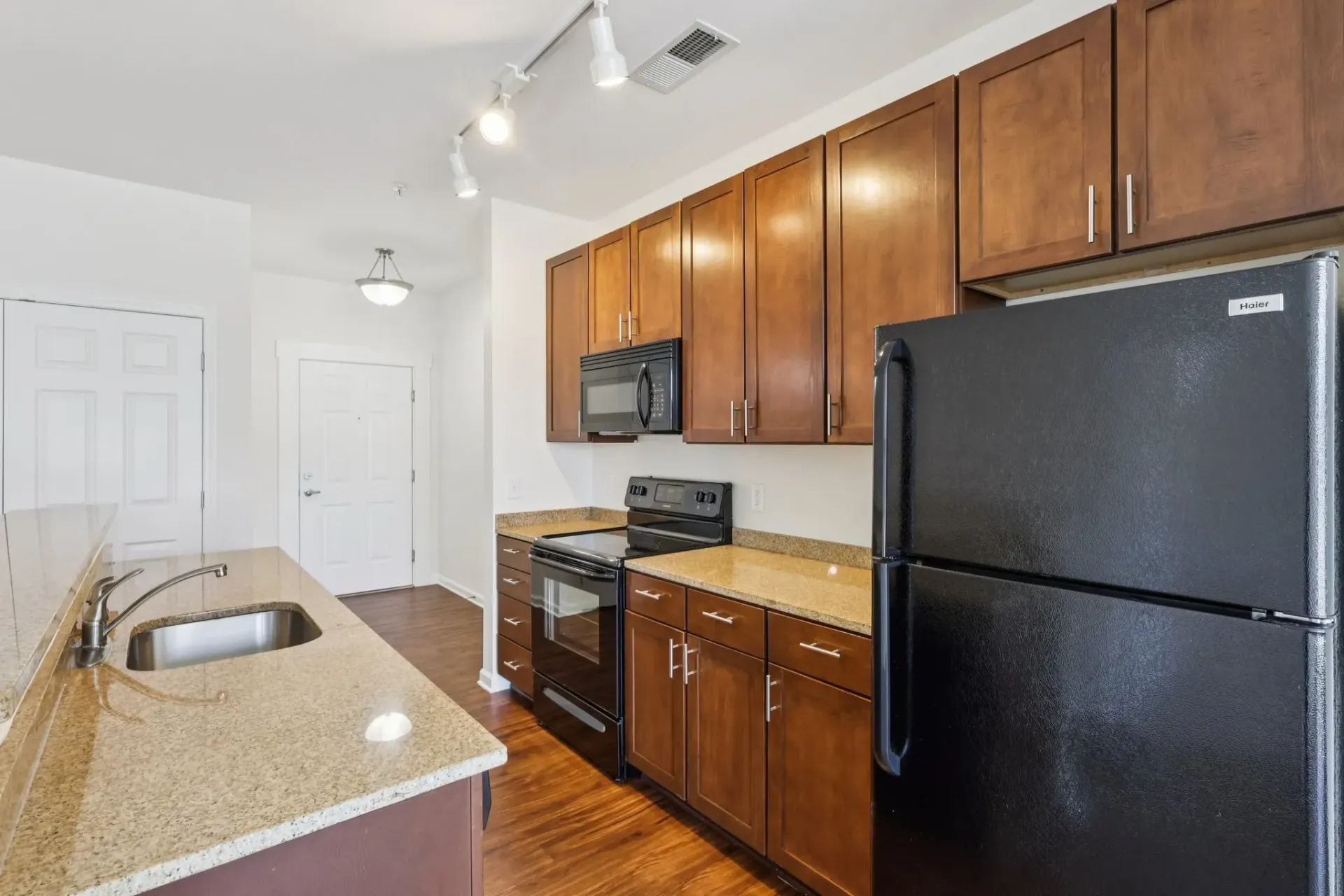Kitchen with granite countertops, stainless steel sink, wooden cabinets, black appliances, and a doorway.