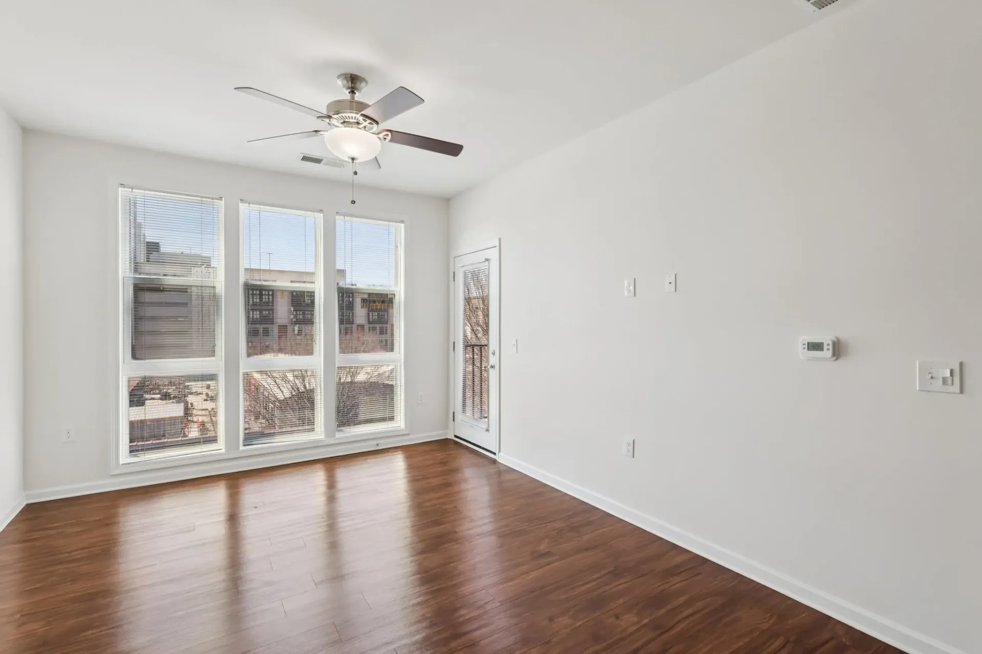 Living room with hardwood floors, large windows, and a ceiling fan.