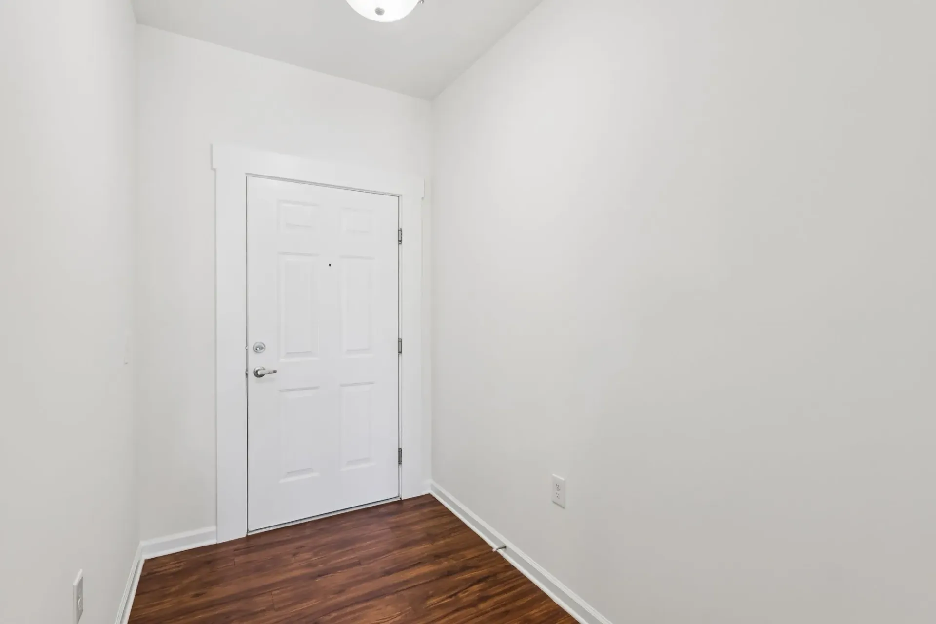 Interior view of an apartment entrance door with white walls and wooden floor.