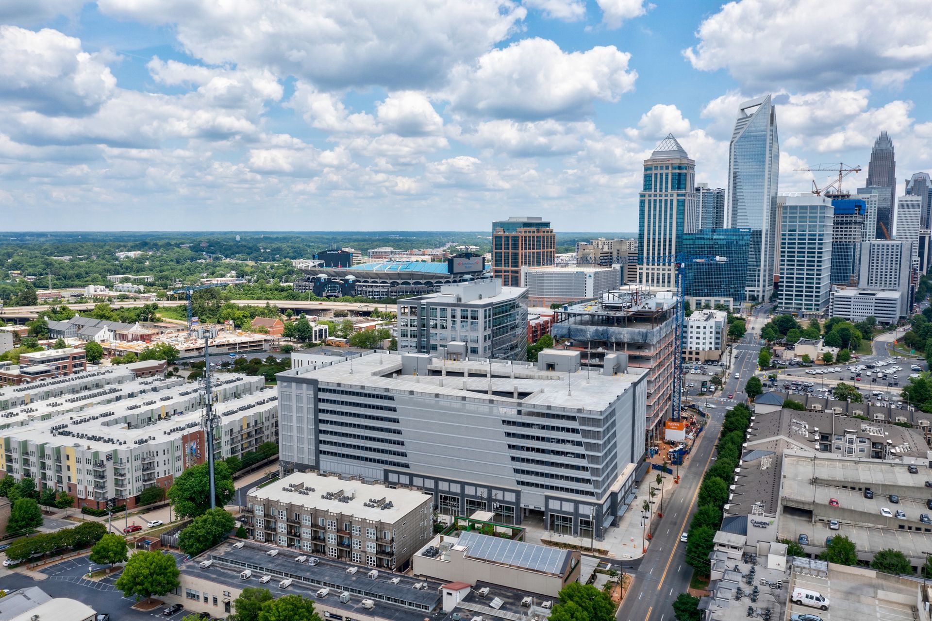 Aerial view of Charlotte, NC skyline with tall buildings, parking garage, and residential areas under a cloudy sky.