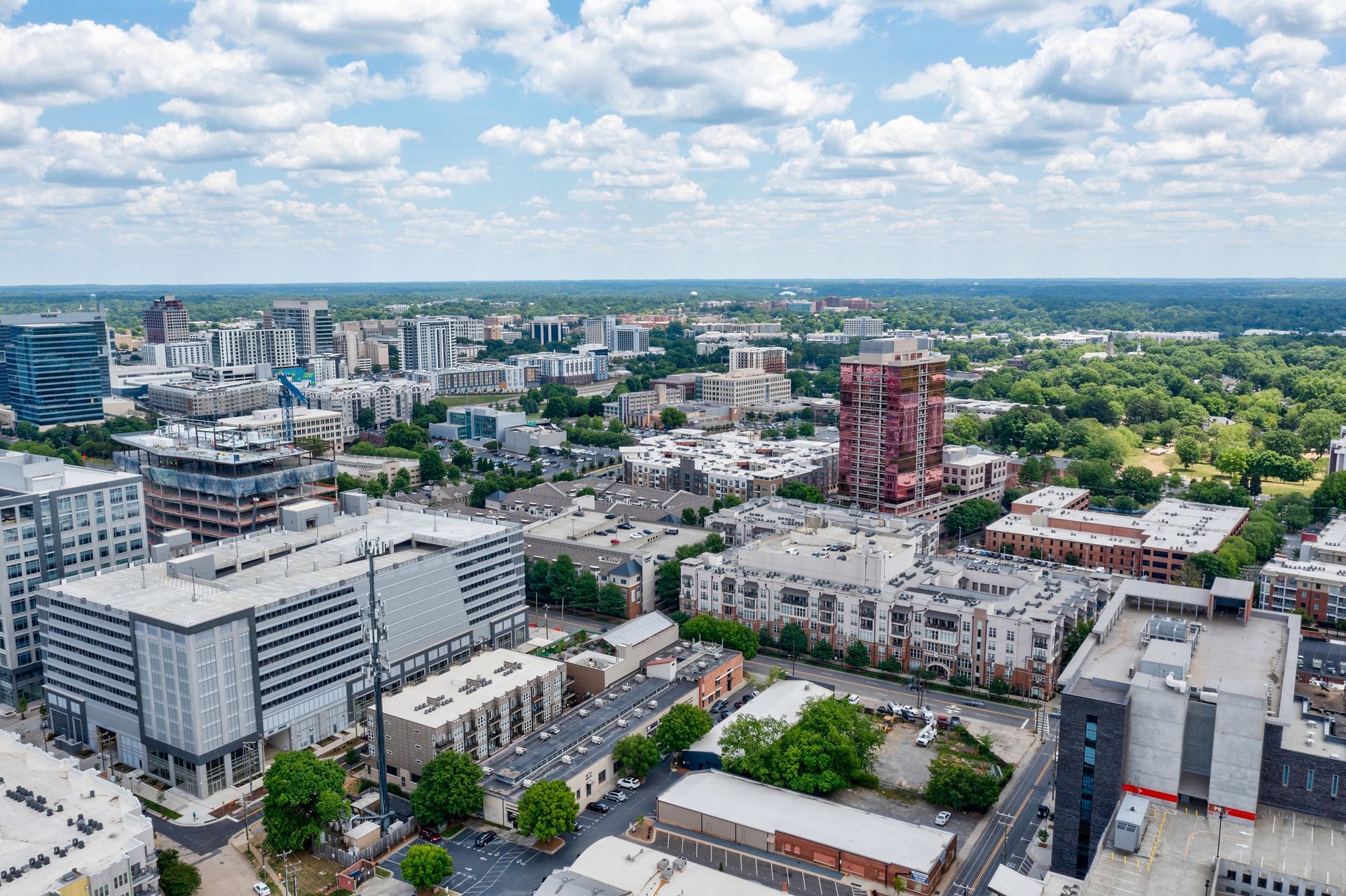 Aerial view of a city with buildings, trees, and a blue sky with clouds.