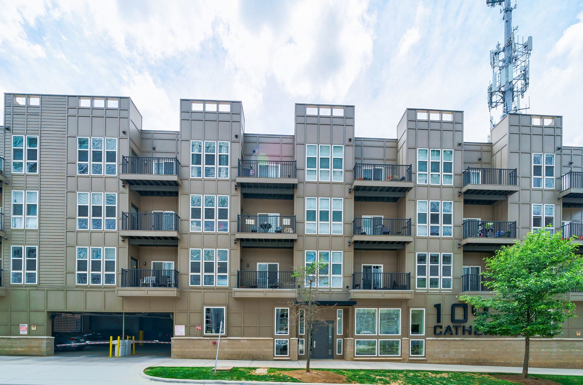 Modern apartment building exterior with balconies, brown facade, cloudy sky, and a cellular tower.