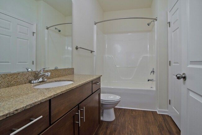 Bathroom with brown vanity, white tub/toilet, and wood-look flooring.
