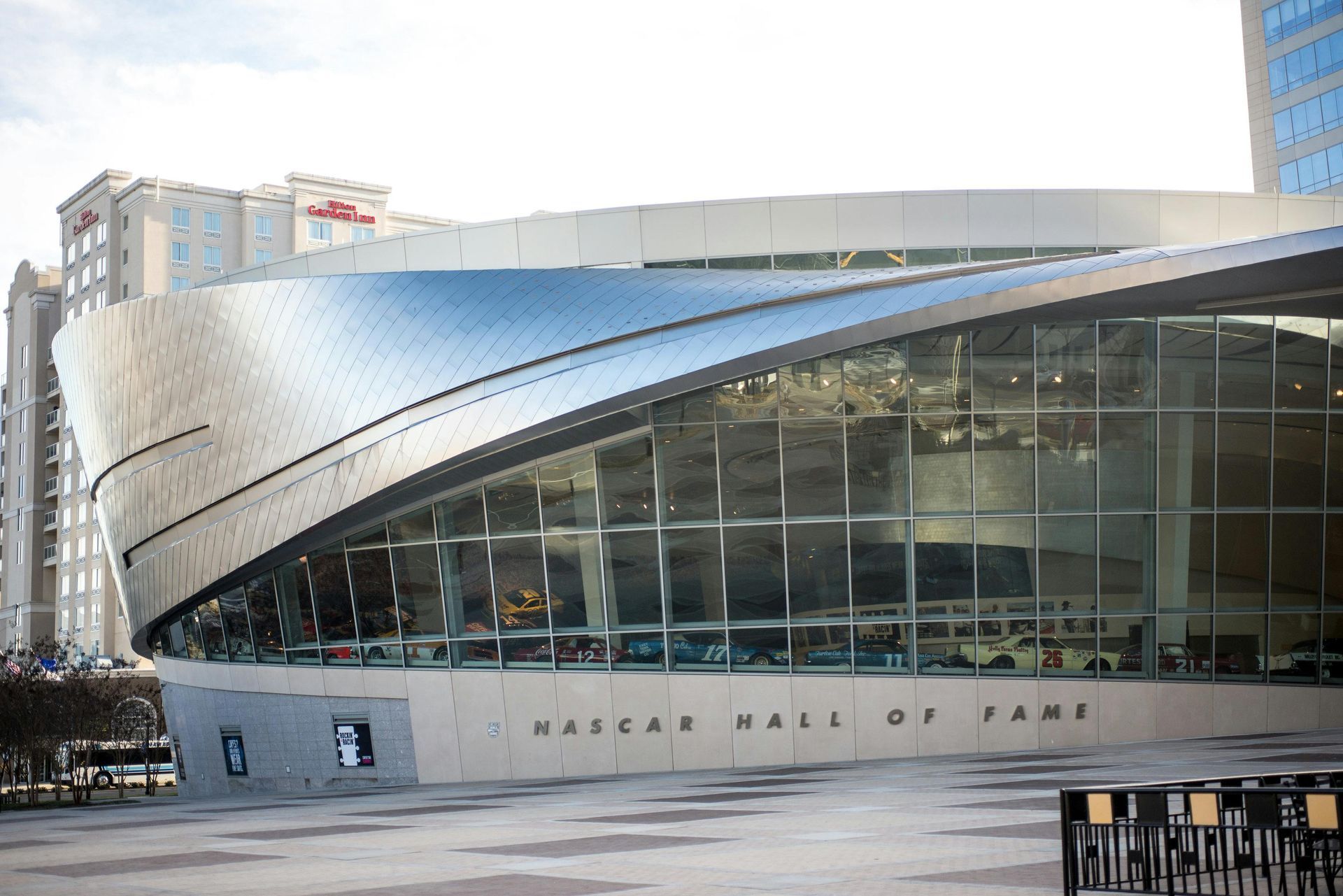 The NASCAR Hall of Fame building in Charlotte, featuring a curved, modern silver roof and a large glass-walled facade.