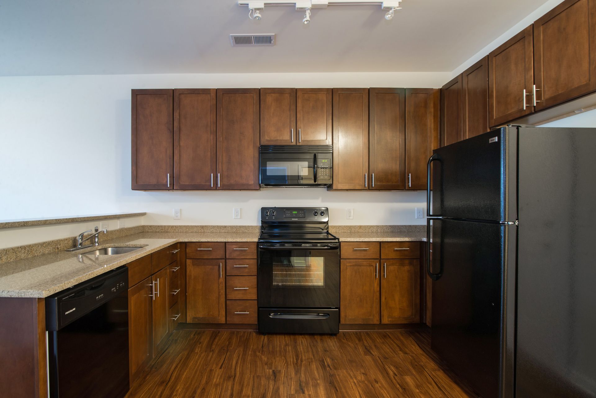 A kitchen with brown wooden cabinets, black appliances, speckled countertops, and wood-patterned flooring.
