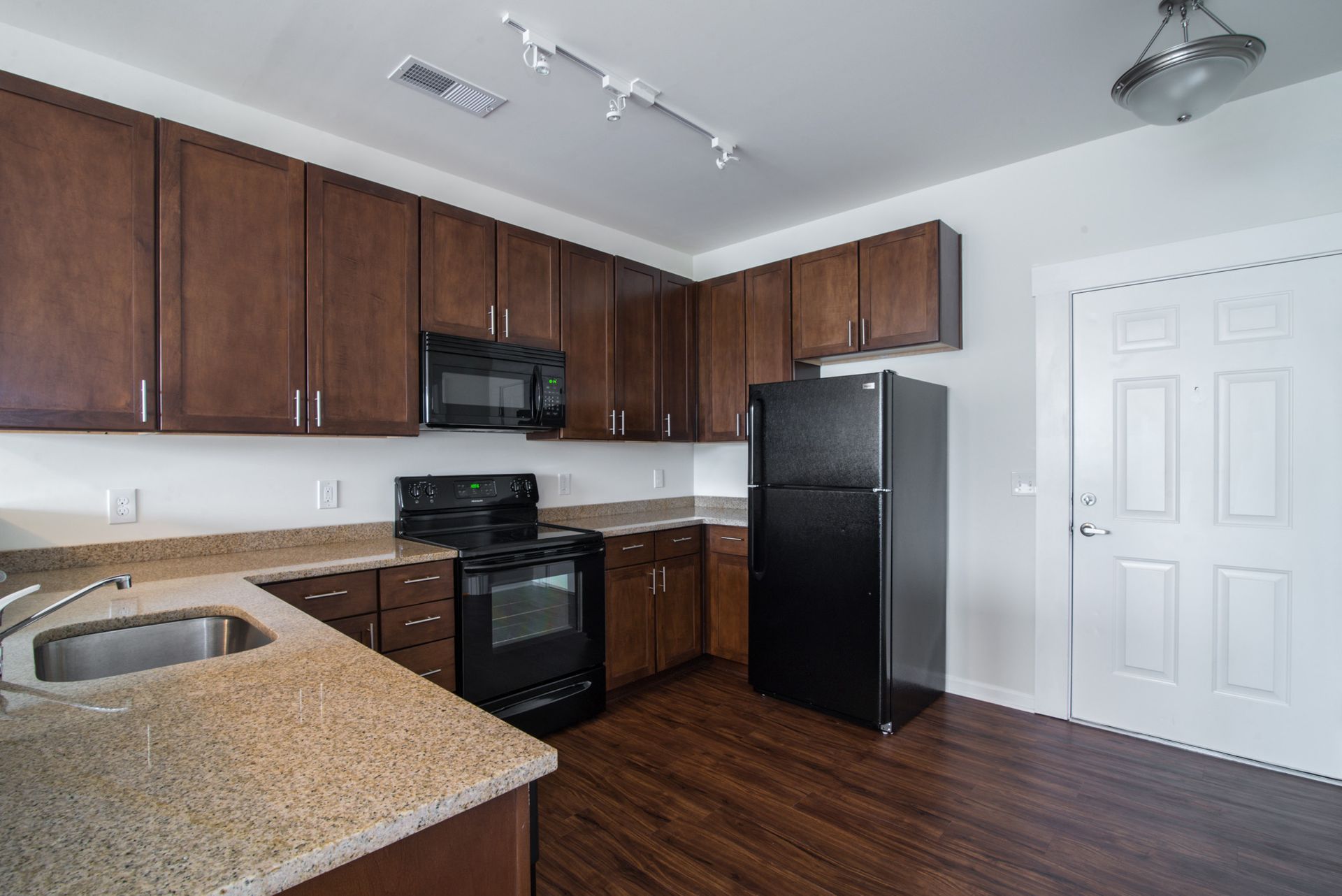 Modern kitchen featuring dark wood cabinets, black appliances, granite countertops, and wood-style flooring.