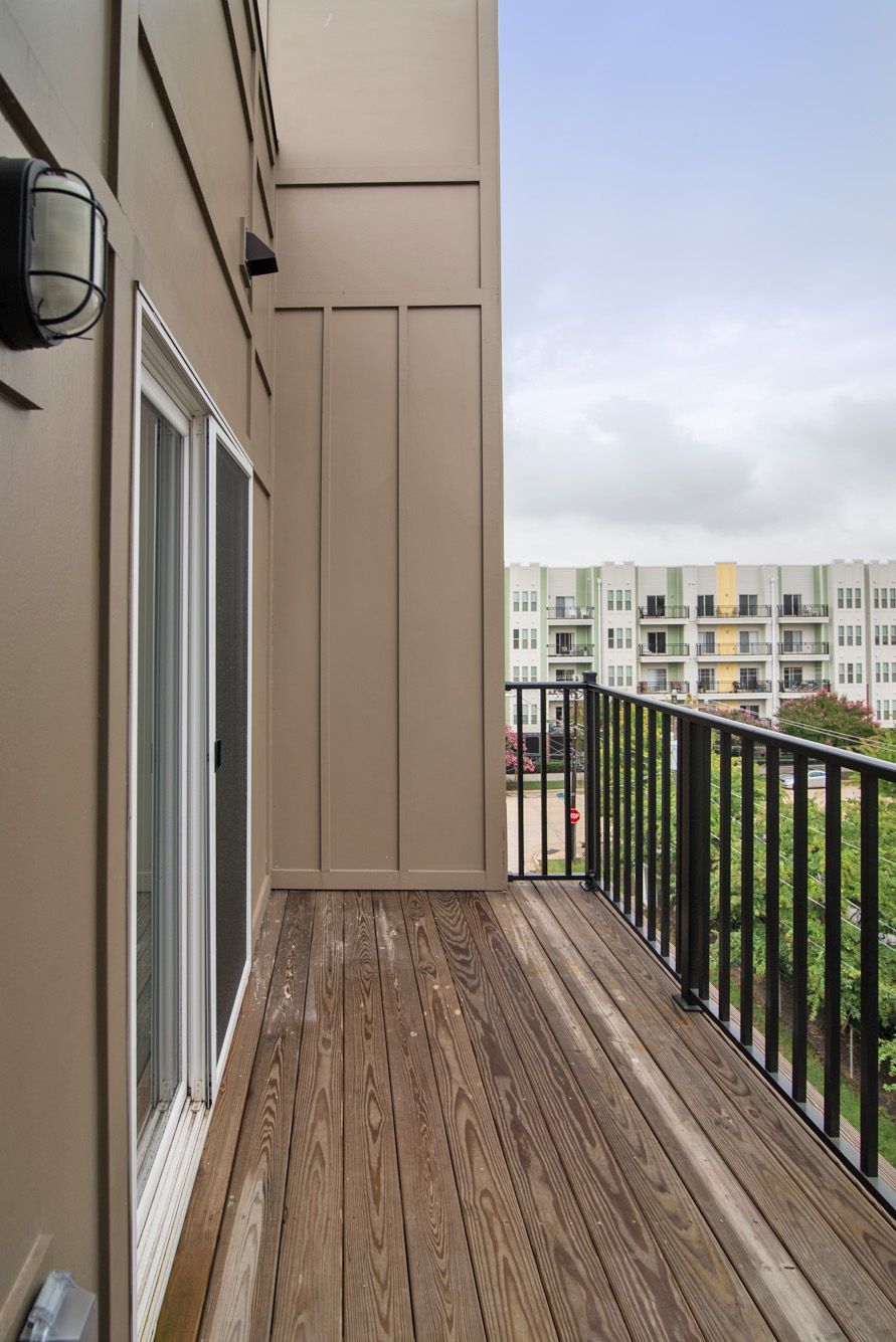 A wooden balcony with a black railing, overlooking an apartment complex under a cloudy sky.