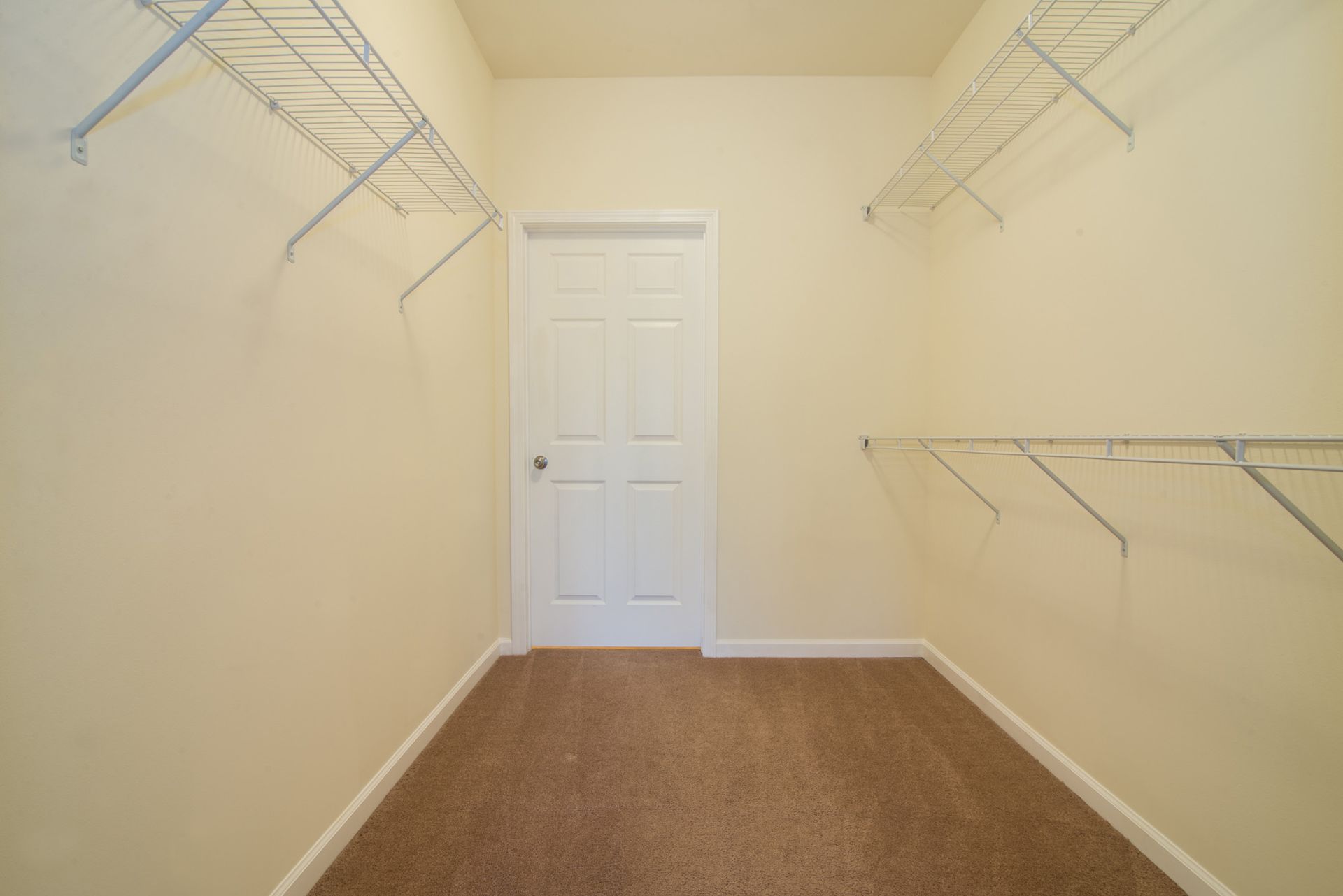Empty walk-in closet with beige walls, brown carpet, and white wire shelving on both sides.
