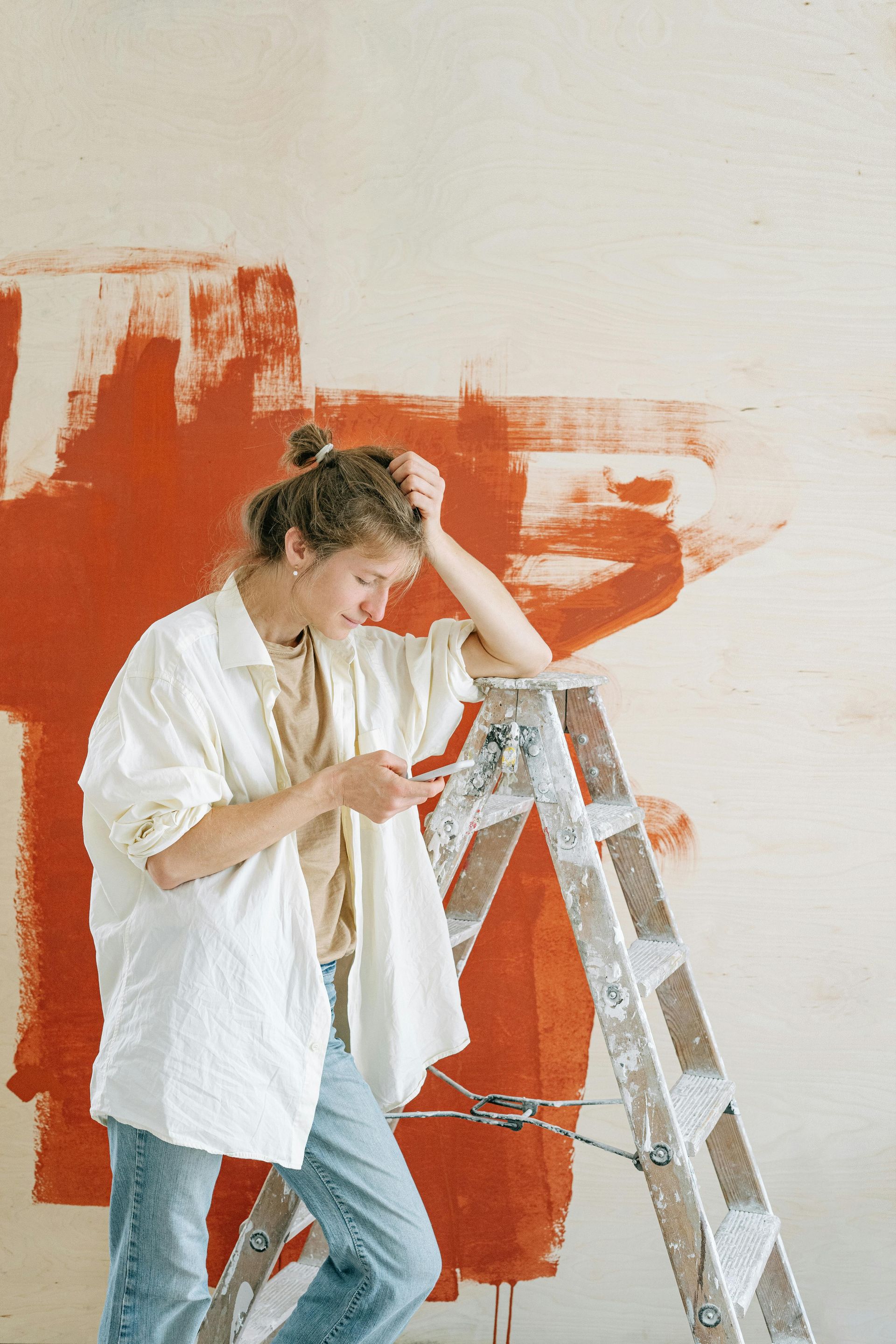 A woman is standing on a ladder in front of a red wall.