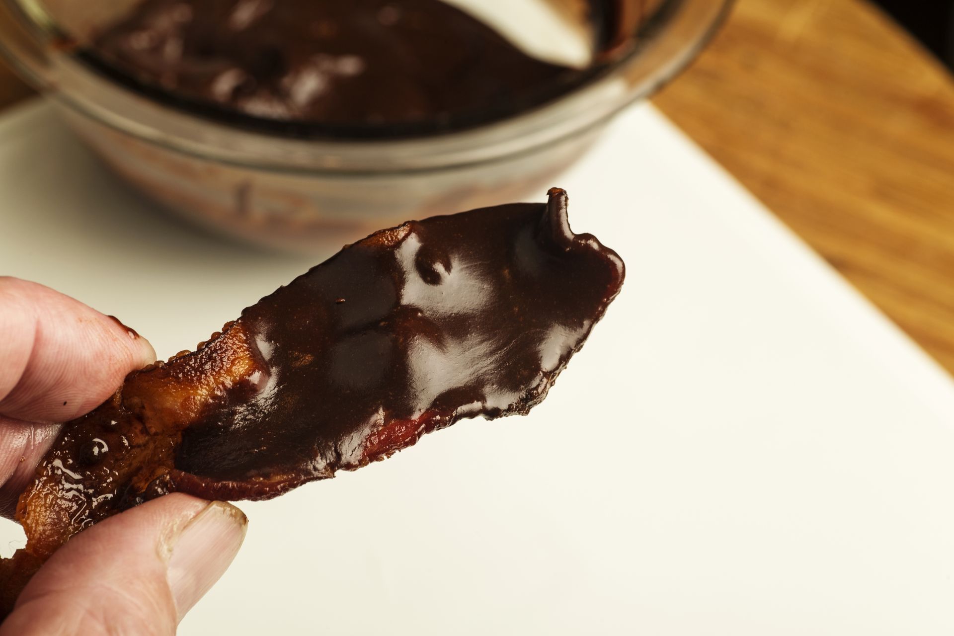 Hand holding a strip of bacon coated in dark chocolate