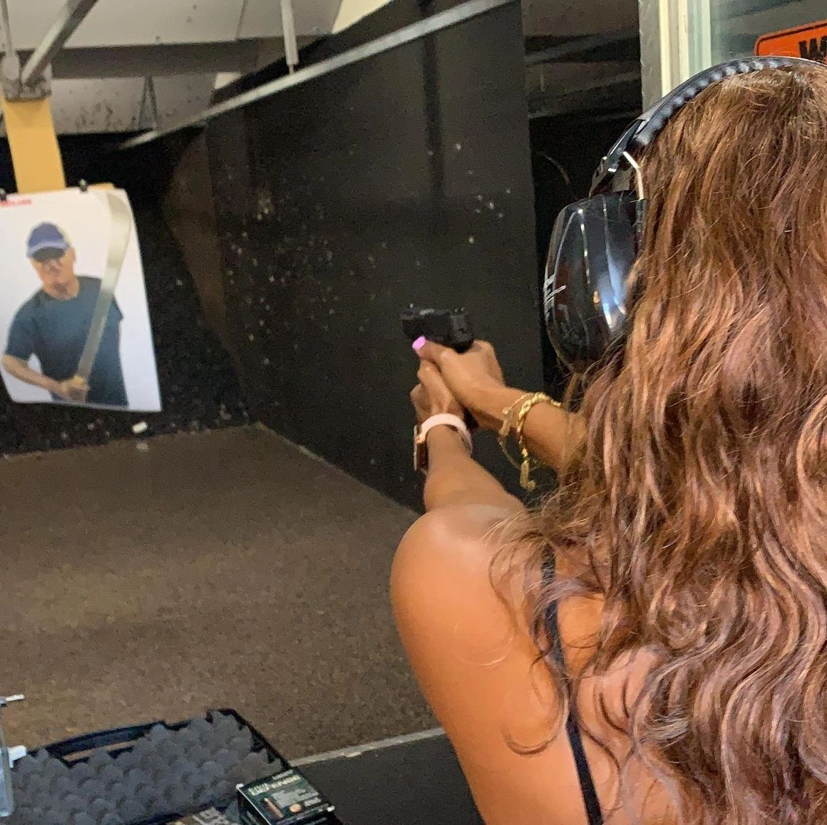 Woman shooting a handgun at a target in a gun range. She wears hearing protection and holds the gun with both hands.