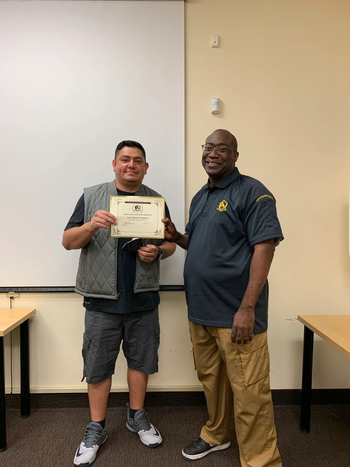 Man receiving a certificate from another man in a room with tables.