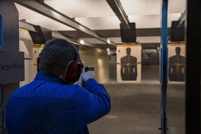 Man shoots handgun at targets in an indoor shooting range.