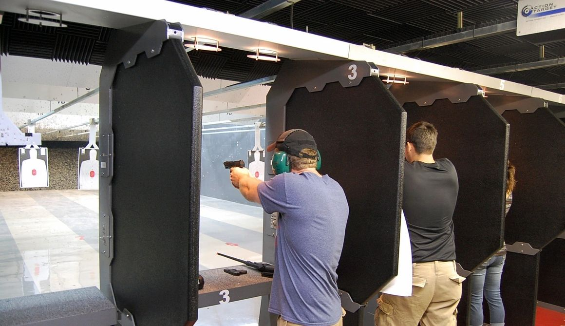 People shooting handguns at an indoor shooting range, wearing ear and eye protection.