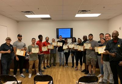 Group of people holding certificates, smiling in a brightly lit room.