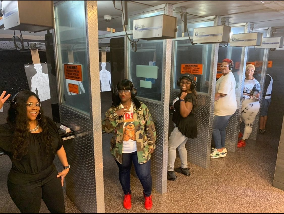 Group of people at an indoor shooting range; targets, safety glasses, holding or posing near firing lanes.