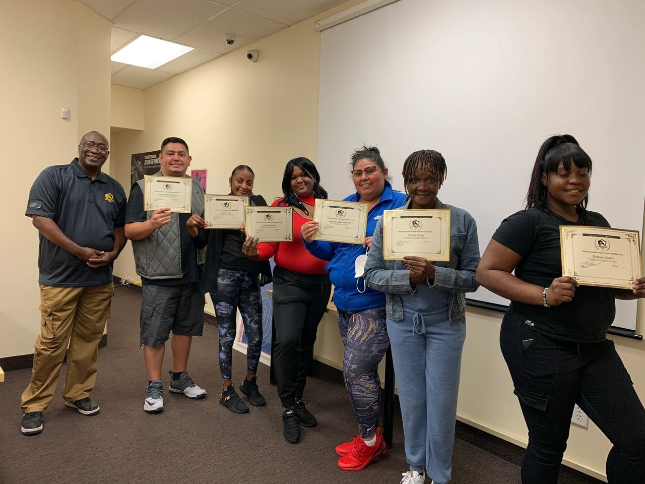 Group of people holding certificates, smiling in a room with a projector screen.