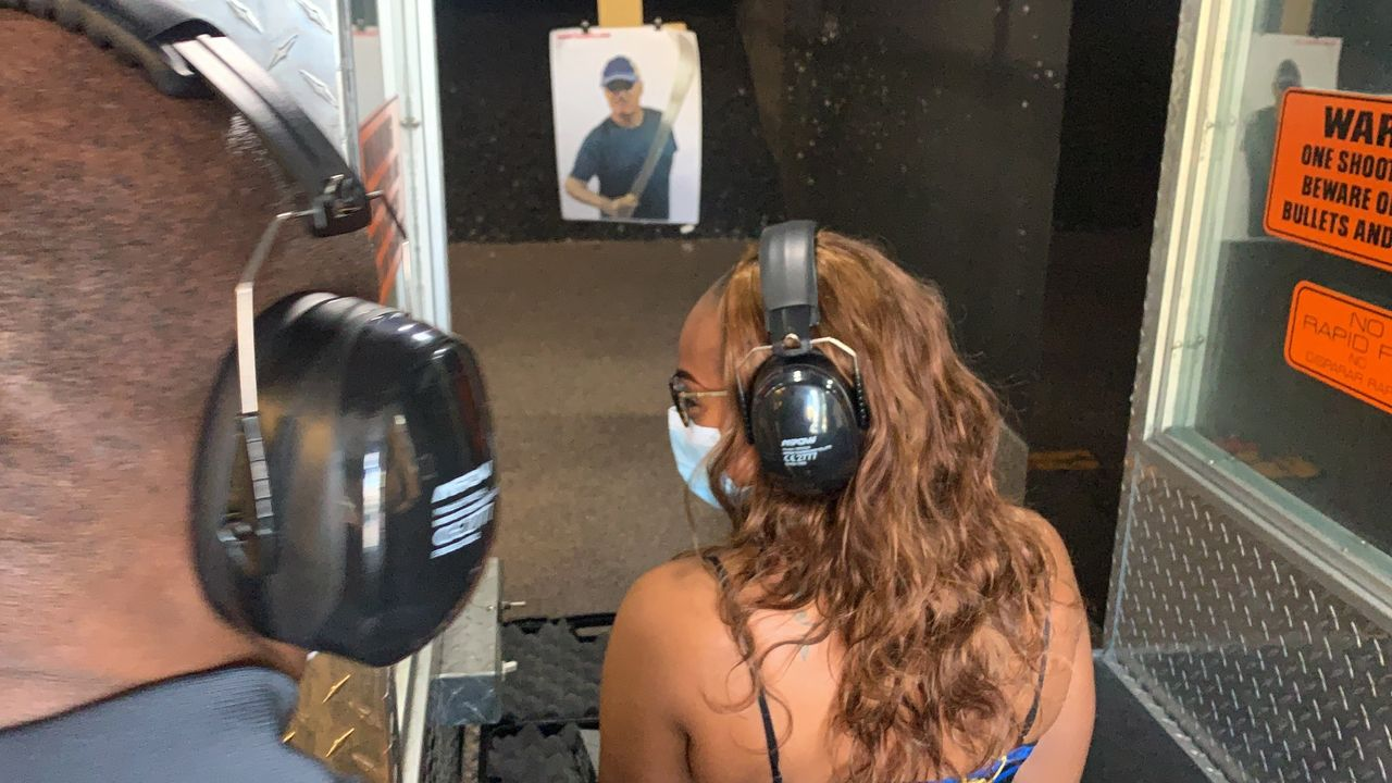 Two people with earmuffs and a face mask at a shooting range, aiming at a target.