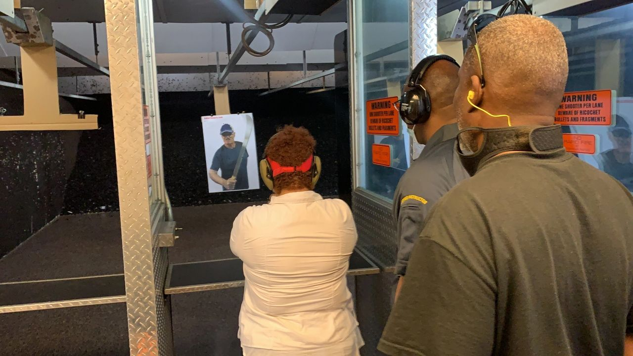 Woman shooting a handgun at a target in a shooting range, with two spotters.