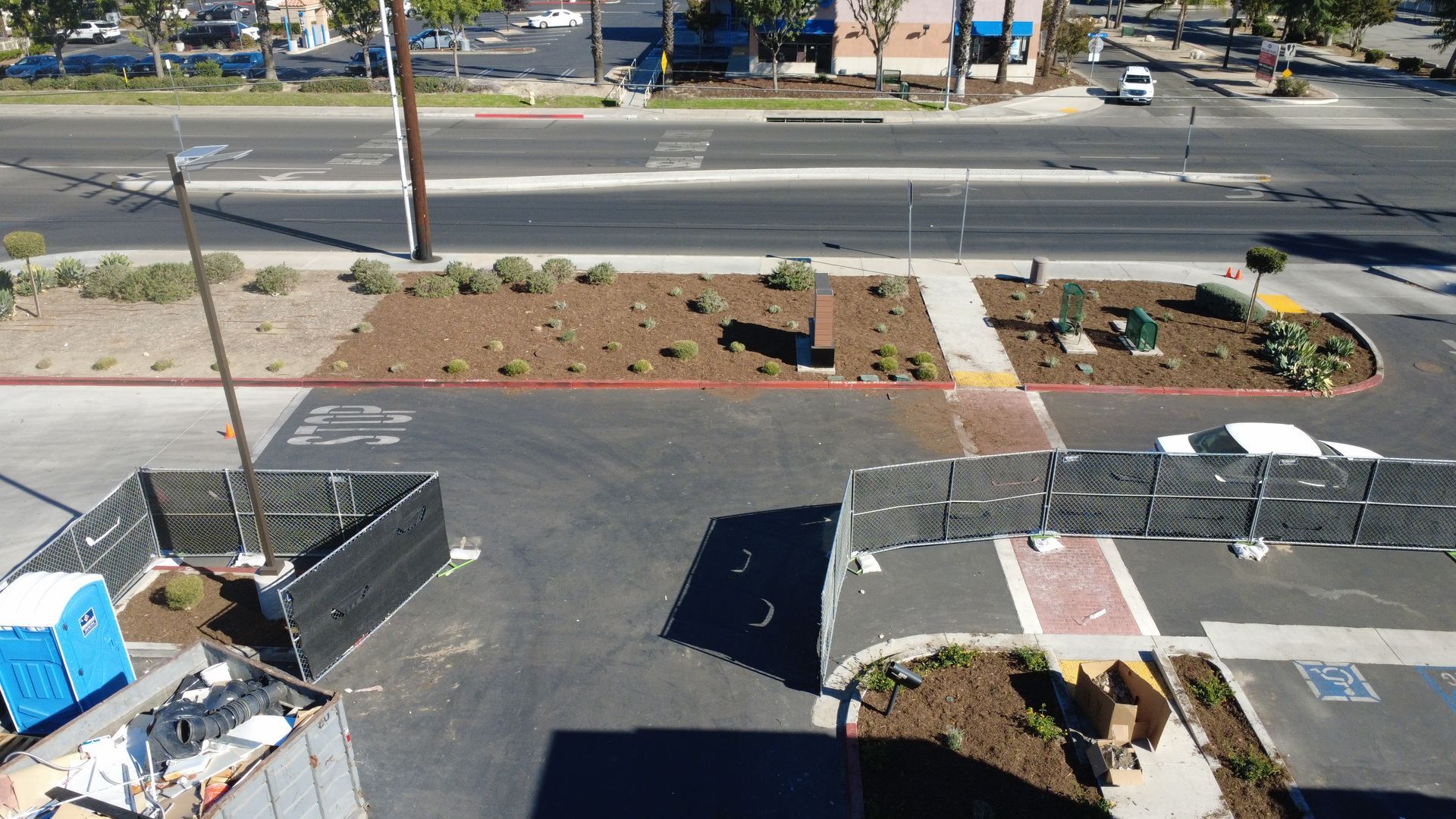 Overhead view of a parking lot with landscaping, construction fencing, and a street with traffic.
