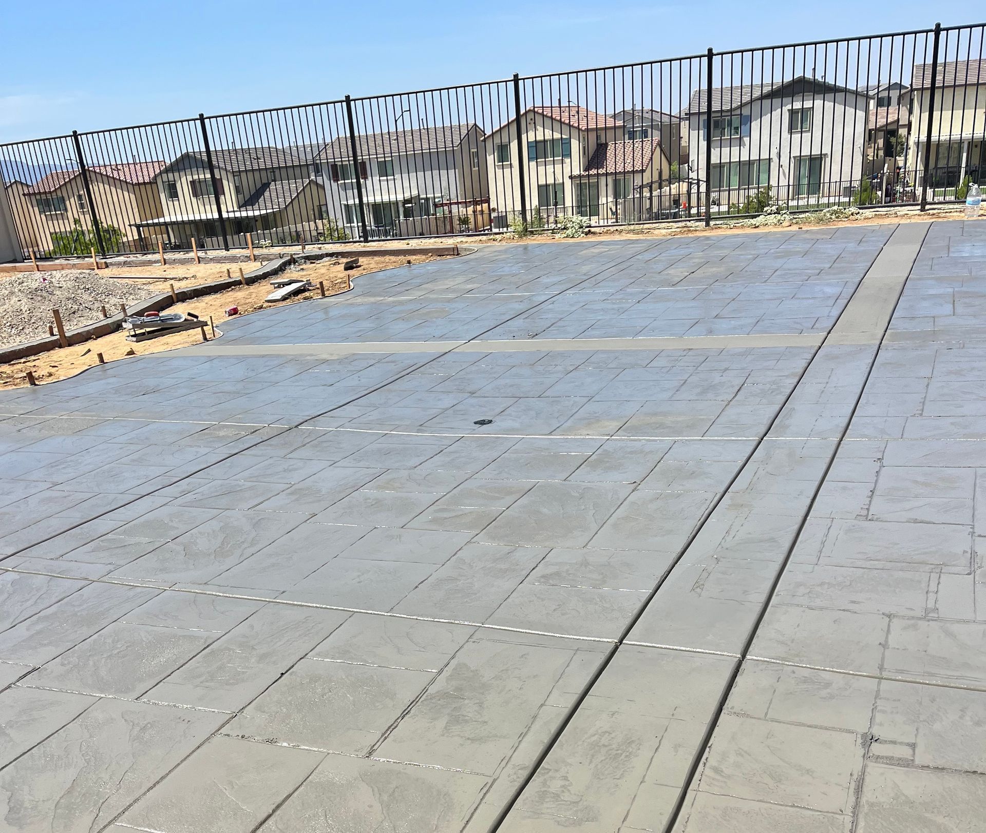A fence surrounds a large concrete area with houses in the background