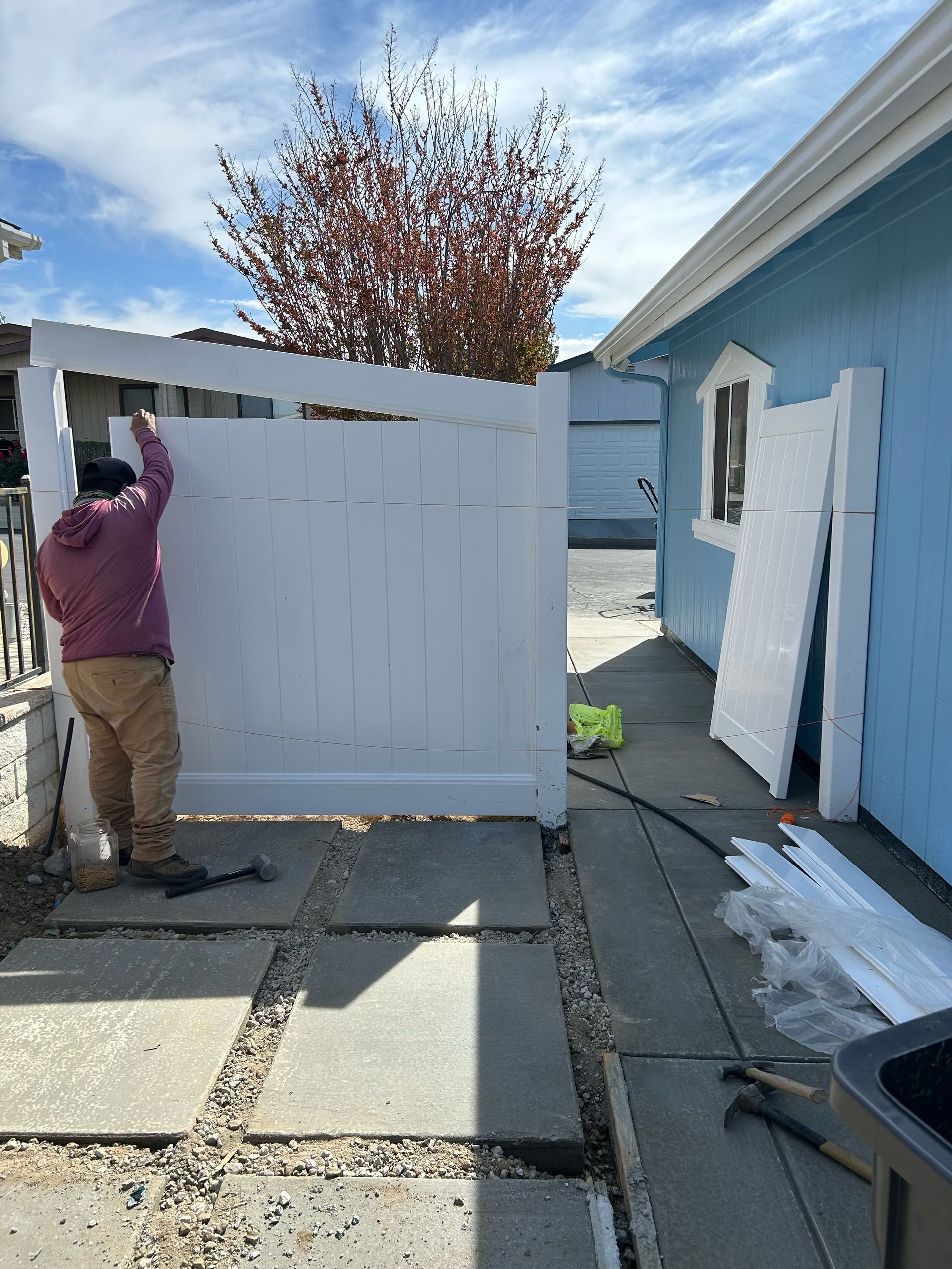 A man is installing a white fence in front of a blue house.