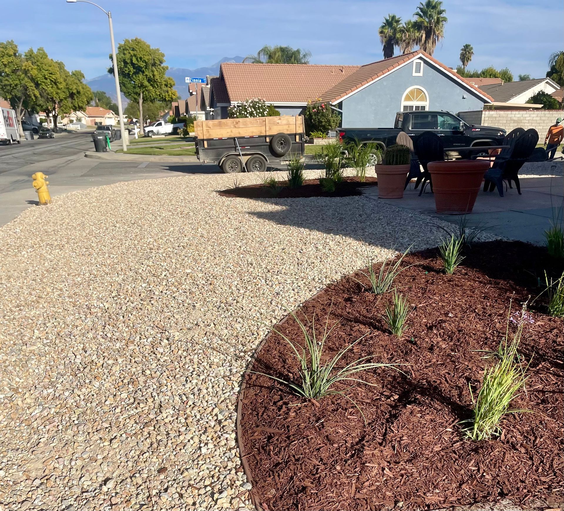 Gravel and mulch landscaping on a residential street. Brown mulch surrounds new plants; beige gravel covers the larger area.