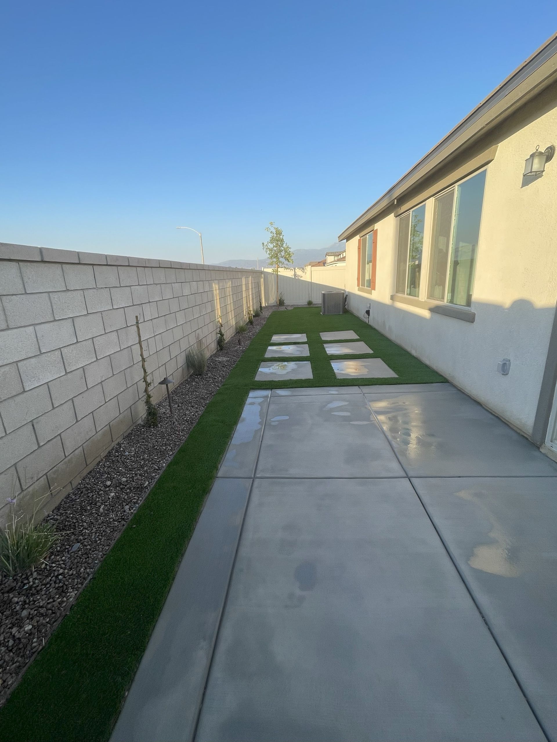 Backyard with concrete patio, grass strip, stepping stones, and a block wall.