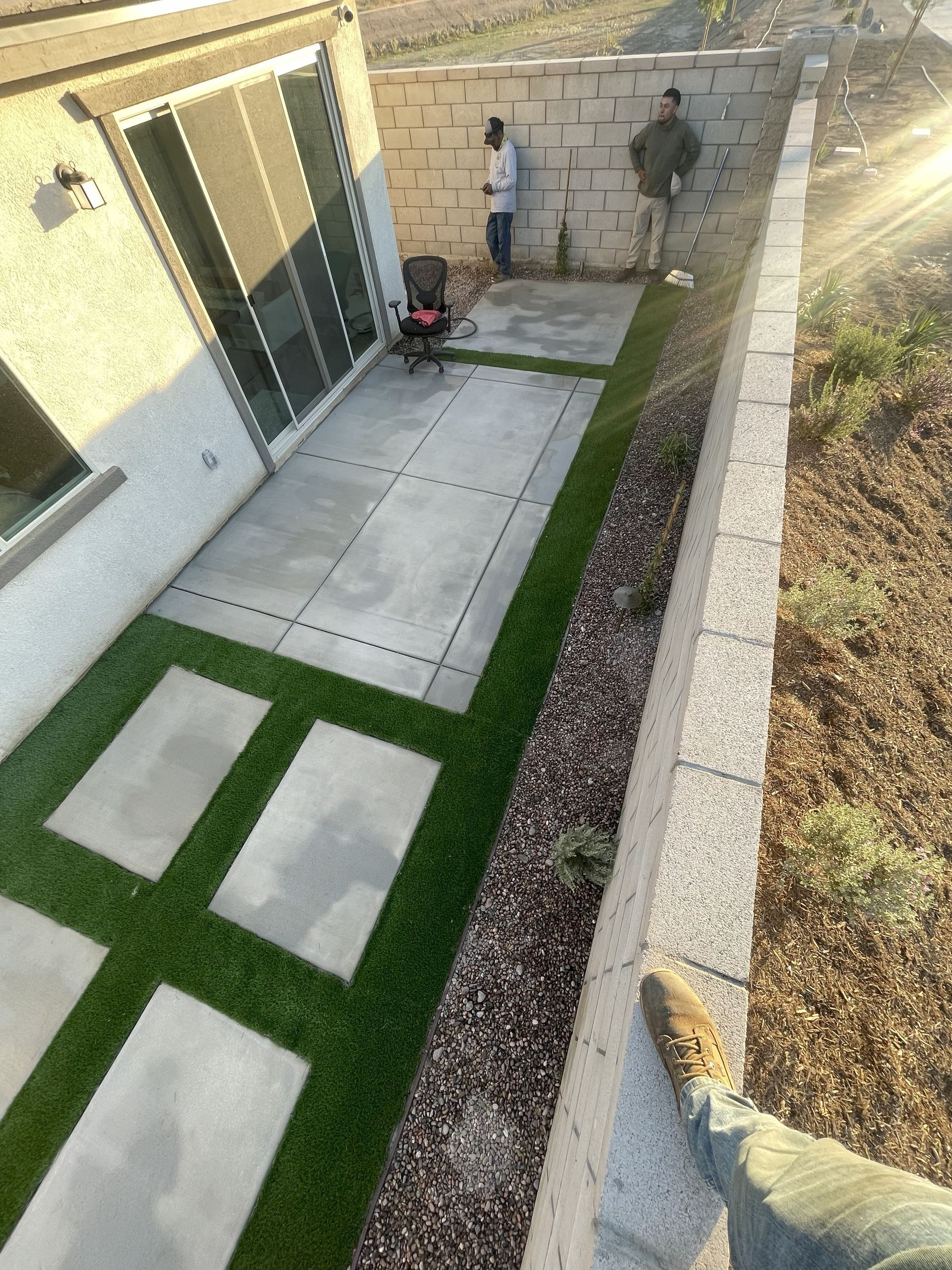 Patio with concrete pavers, artificial turf, and workers by a retaining wall.