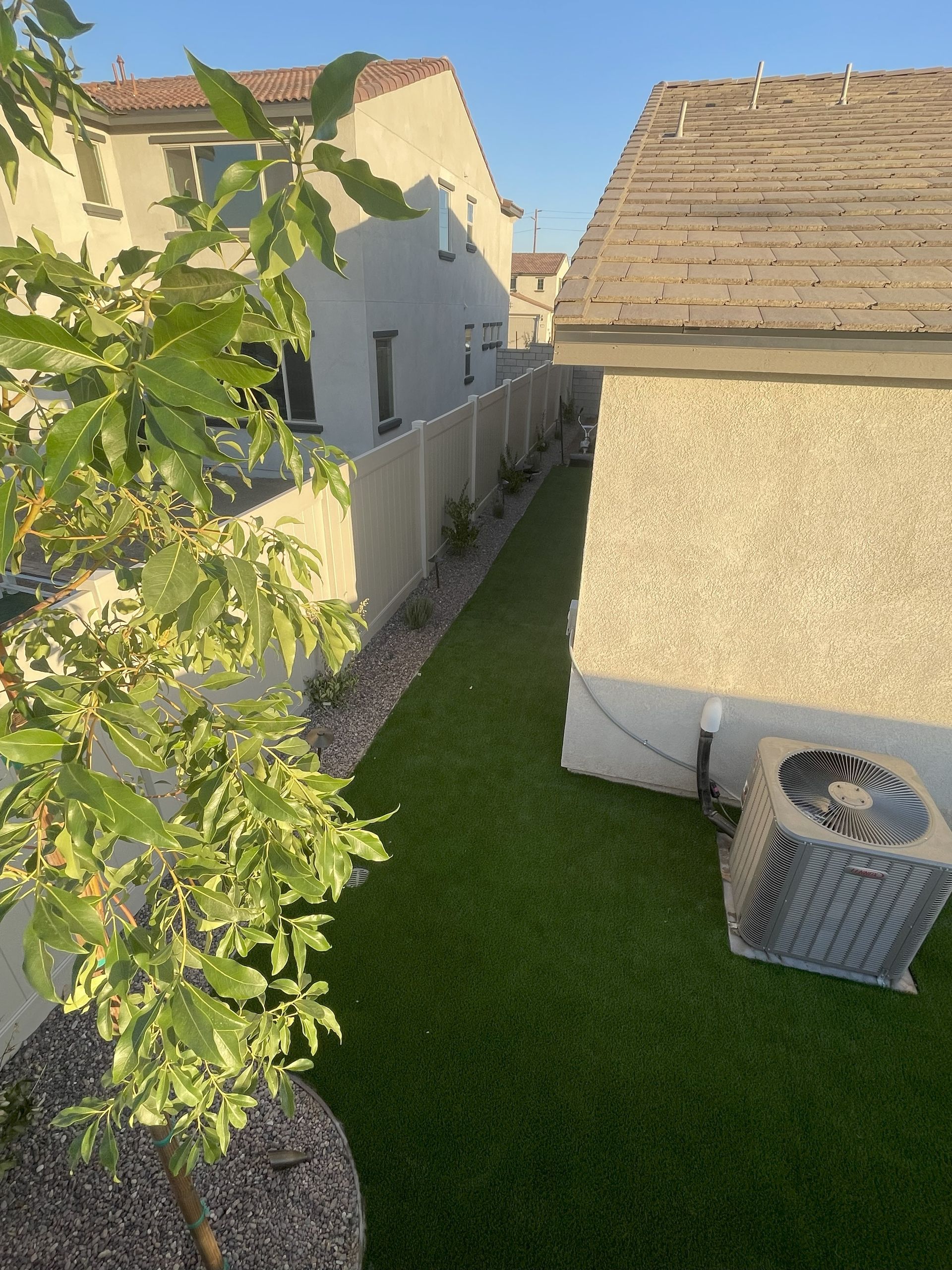 Narrow backyard with artificial turf, white fence, beige houses, and an AC unit.