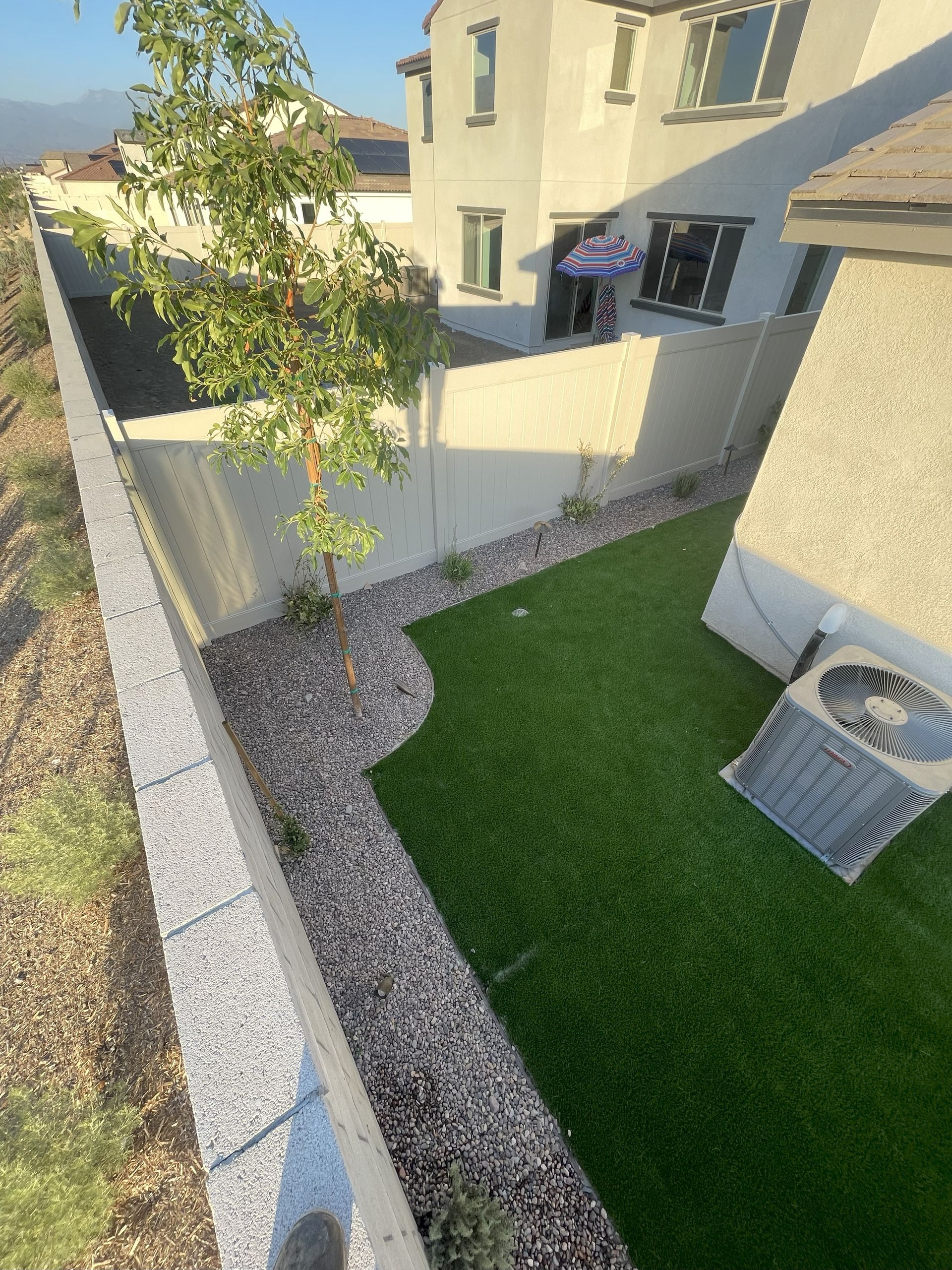 Backyard with artificial turf, gravel path, and tall concrete wall beside a two-story house.